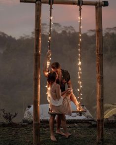 a man and woman kissing on a swing with string lights hanging from the ceiling in front of them