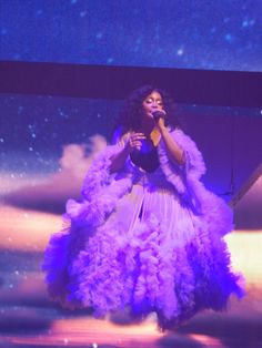 a woman standing on top of a stage in front of a purple backdrop holding a microphone