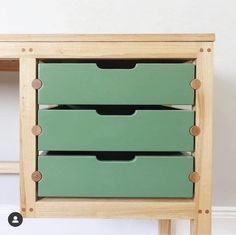 two green drawers are on top of a wooden table with white walls in the background