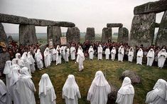 a group of people dressed in white standing next to each other near stonehenge