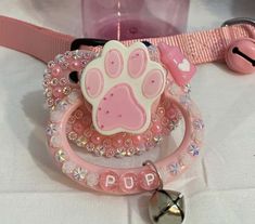 a pink pacifier with a paw print on it and a bell attached to it