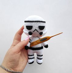 a hand holding a tiny crocheted star wars character with a pair of scissors