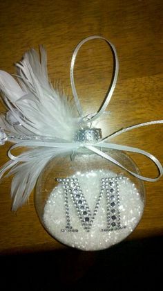 a glass ornament decorated with white feathers and beads on a wooden table top