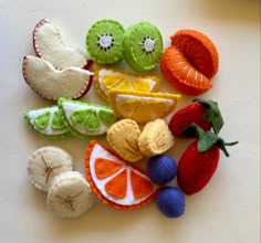 felt fruits and vegetables are laid out on a white surface, including oranges, kiwis, lemons, strawberries, and grapes