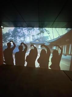 silhouettes of people standing in front of a screen with trees and buildings behind them