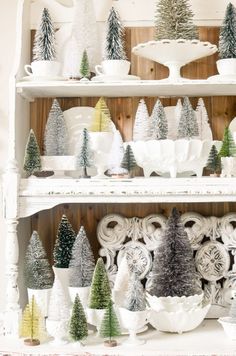 christmas trees are displayed on shelves in a room with white dishes and other decor items