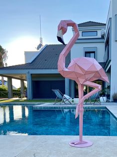 a pink flamingo standing next to a swimming pool in front of a large house