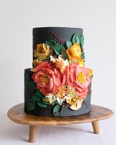 a multi - layered cake decorated with flowers and leaves on a wooden stand against a white wall