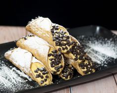 some pastries are on a black plate with powdered sugar and sprinkles