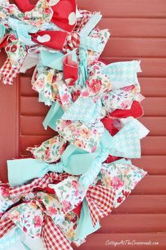 a wreath made out of fabric with hearts and flowers on the side of a red door