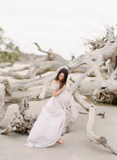 a pregnant woman standing in front of driftwood on the beach