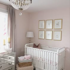 a baby's room with pink walls and white crib in the corner, chandelier above