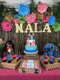 a table topped with cakes and cupcakes next to a wall covered in paper flowers