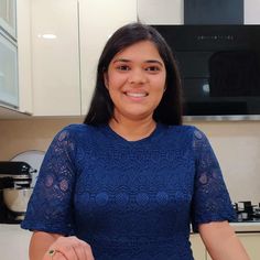 a woman standing in a kitchen holding a plate with food on it and smiling at the camera