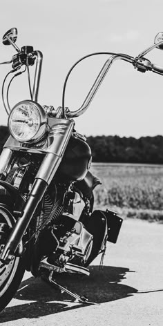 a black and white photo of a motorcycle parked on the side of the road with no one around it