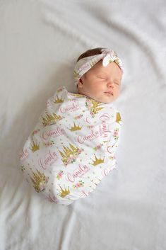 a baby wrapped in a pink and gold crown sleeping on top of a white blanket