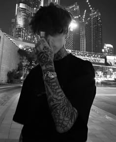 a man with tattoos on his arm is talking on the phone in front of a cityscape