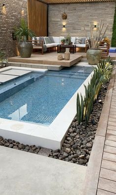 a small pool surrounded by rocks and plants in a backyard with an outdoor seating area