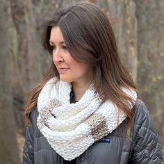 a woman standing in front of trees wearing a white scarf and black jacket with brown trim