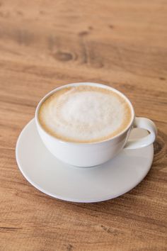 a cappuccino sitting on top of a white saucer next to a wooden table