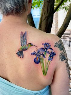 a woman with a tattoo on her back has flowers and a hummingbird in flight