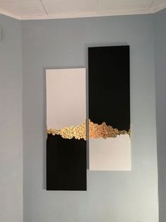 two black and white paintings hanging on the wall in a room with blue walls, one has gold trim