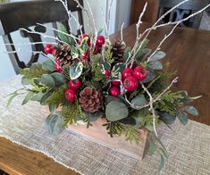 a wooden table topped with a vase filled with red berries and greenery covered in pine cones