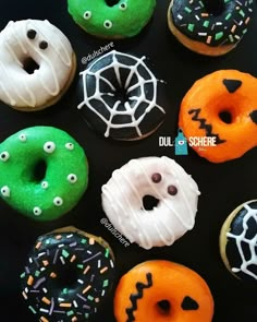 there are many decorated doughnuts on the black table together with sprinkles