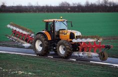 a tractor is plowing the road in front of a green field with two rows of crops