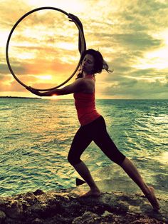 a woman holding a hoop on top of a rock near the ocean