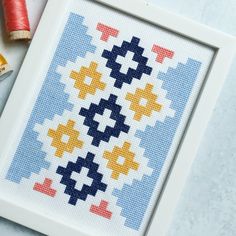 a cross stitch pattern in a white frame next to two spools of thread