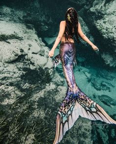 a woman in a mermaid costume is swimming through the water with fish tails on her back