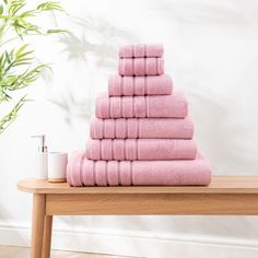 a stack of pink towels sitting on top of a wooden table next to a plant