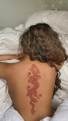 a woman laying in bed with a tattoo on her back