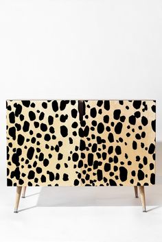 an animal print sideboard with wooden legs and black spots on the front, against a white background