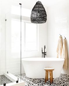 a white bath tub sitting under a window next to a wooden stool in a bathroom