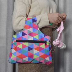 a woman holding a multicolored purse with a crochet hook in her hand