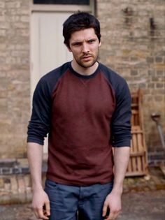 a man standing in front of a brick building with his hands on his hips and looking at the camera