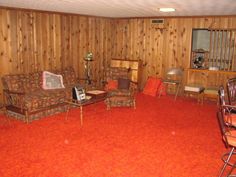 a living room filled with furniture and red carpeted flooring in front of wooden walls