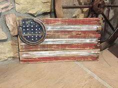 an old wooden american flag is displayed on a stone wall next to a spinning wheel