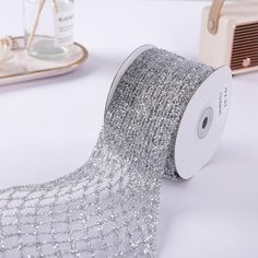 a roll of silver sequinized ribbon on a white table next to other items