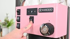 a person pressing buttons on a pink coffee machine