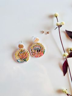 Add a pop of color and playfulness to any outfit with our Handpainted Protea Earrings. These unique earrings feature a fun design on the back and come in two options: with or without black accents. Made with high quality 925 silver stud posts and handcrafted from durable polymer clay. Artistic White Drop Earrings, Artsy White Drop Earrings, Artsy White Pierced Earrings, Artsy White Earrings, Artistic Hand Painted White Earrings, White Artsy Earrings With Ear Wire, Artsy White Earrings With Ear Wire, Bold Polymer Clay Earrings As Gift, Bold Polymer Clay Earrings For Gift