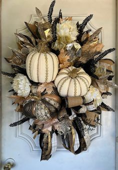 a wreath with white pumpkins and flowers hanging on the front door