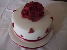 there is a white cake with red roses on the top and bottom, sitting on a table