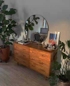 a wooden dresser topped with a mirror next to a potted plant on top of a hard wood floor