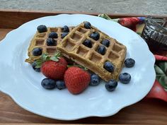 two waffles on a plate with strawberries and blueberries next to it