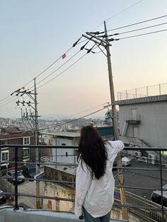 a woman standing on top of a roof next to power lines and telephone poles in the city