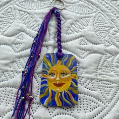 a keychain with a sun painted on the front and purple tassels