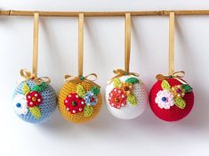 four crocheted apples hanging from hooks on a white wall with wooden pegs